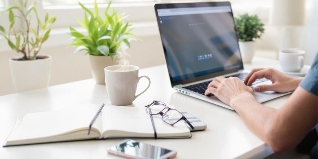Person typing on laptop at home desk with coffee cup