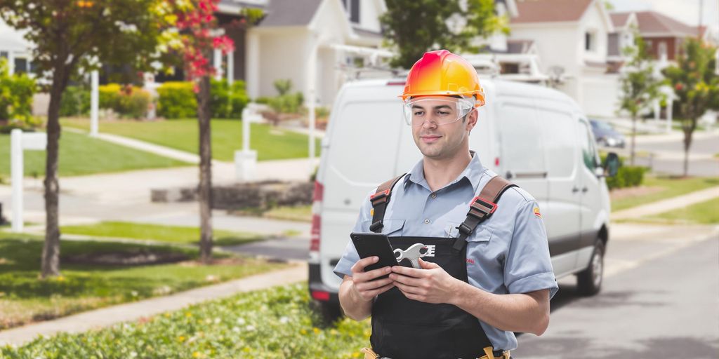 Uniformed plumber holding smartphone and wrench beside suburban service van