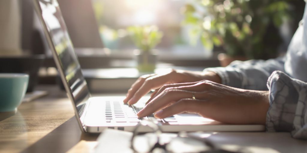 Person typing energetically on a laptop in a bright room.